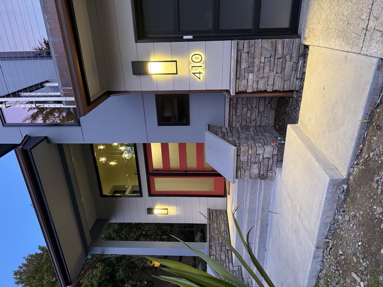 Entry detail at dusk — red door, stacked stone, illuminated house number 410