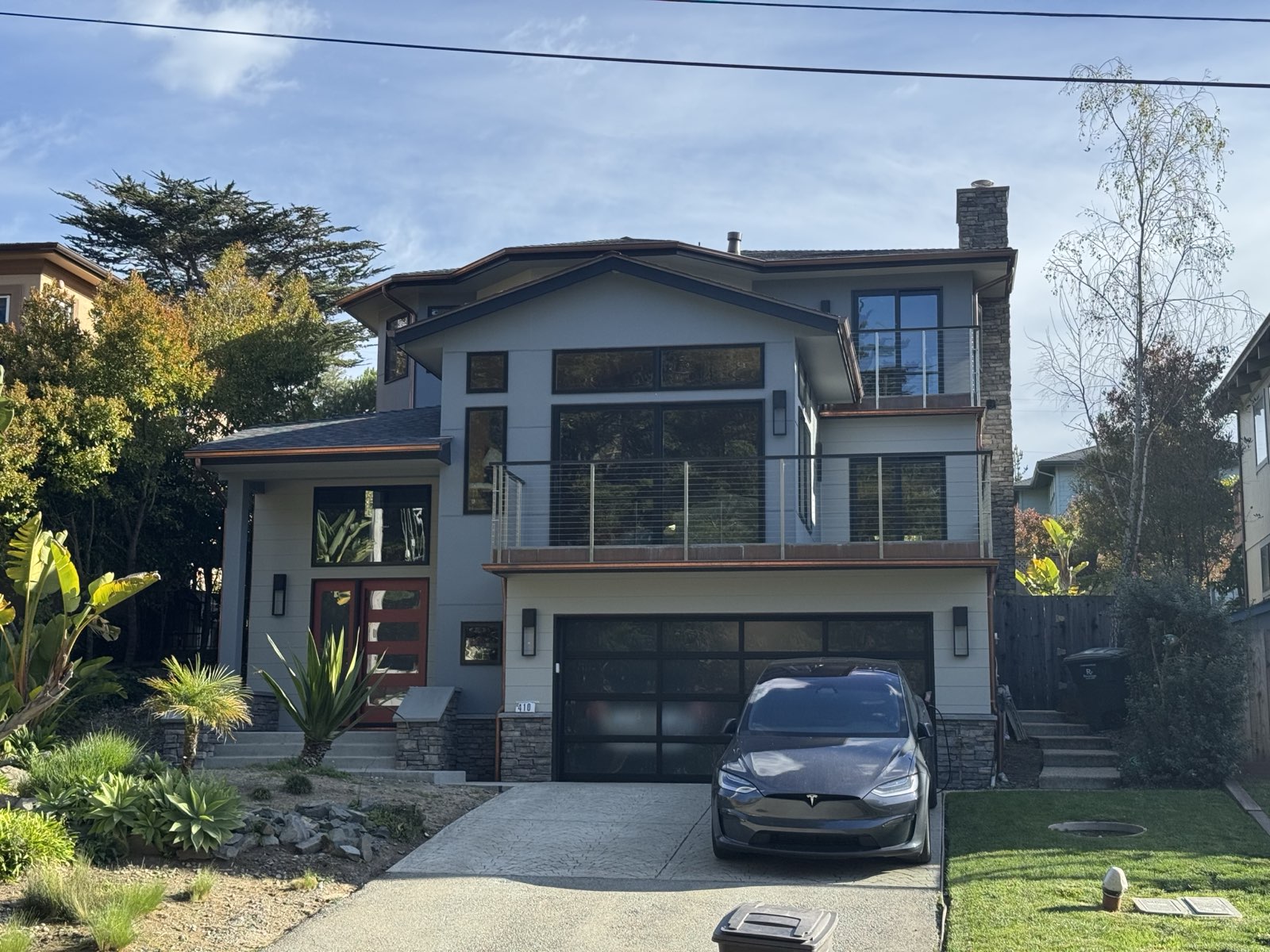 The 410 Residence street elevation in daylight, layered rooflines and stone chimney